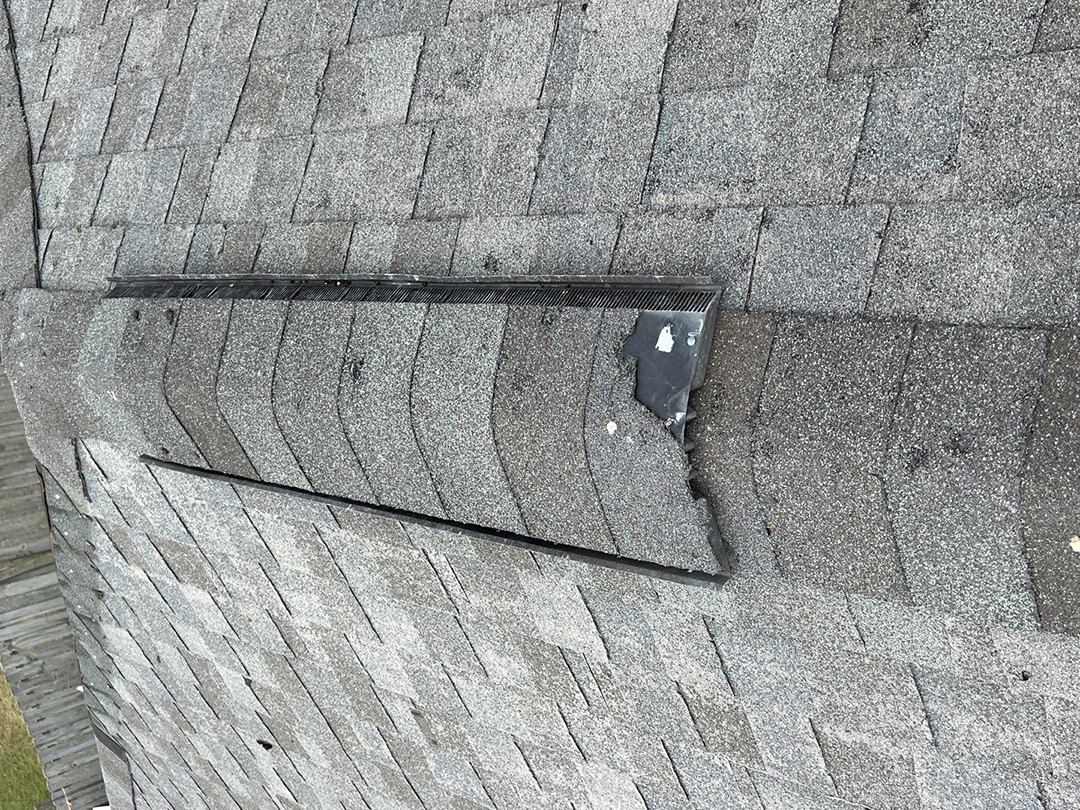 Damaged shingle edge beside a roof ridge