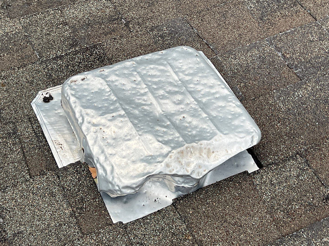Bent metal roof vent cover after hail impact